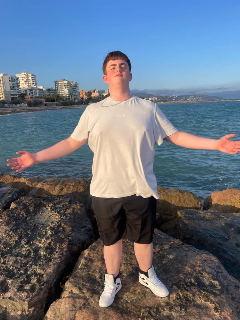 Beau on rocky coastline by the sea, arms open to the horizon